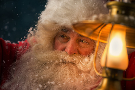 Santa Clause walking outdoors under falling snow with vintage lampの写真素材