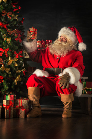 Santa Claus brought gifts for Christmas. Santa is placing gift boxes under Christmas treeの写真素材