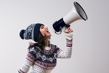 Young winter christmas woman shouting with a megaphone against a white backgroundの写真素材