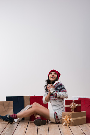 Christmas woman portrait with christmas gifts. Smiling happy girl sitting on wooden floor against white wall background.の写真素材