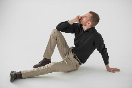 Portrait of handsome young thoughtful man sitting on white background, full lengthの写真素材