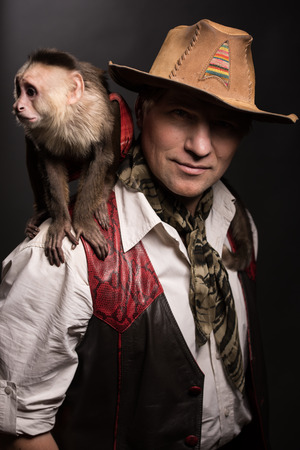 Mature man adventurer in costume of traveler with his monkey companion on black backgroundの写真素材