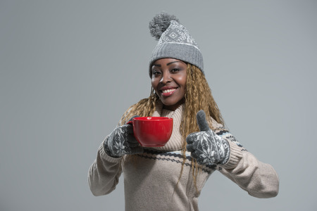 African American woman in winter clothes enjoying a hot drink on gray backgroundの写真素材