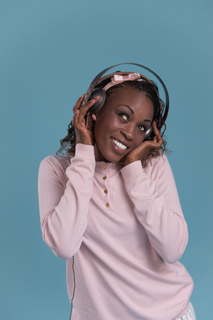 Happy African Woman listening to music on headphones. Young fresh African female model on blue background.の写真素材