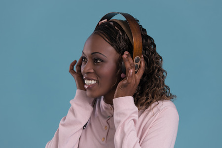 African woman with headphones listening music. Music teenager girl dancing against blue backgroundの写真素材