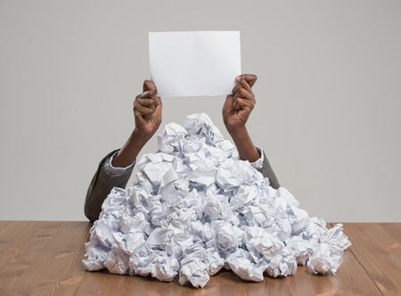 African business woman under crumpled pile of papers with raised hand holding a blank signの写真素材