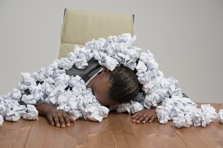 Young african business woman covered in crumpled papers against gray backgroundの写真素材