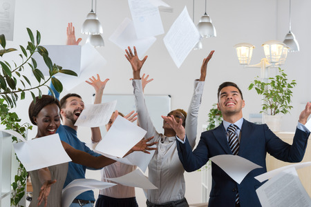 Group of excited multi racial businesspeople throwing papers in officeの写真素材