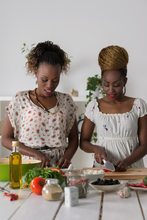 Two african women cooking in kitchen making healthy food salad with vegetablesの写真素材