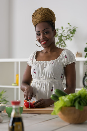 Smiling african woman chopping vegetables for salad at kitchenの写真素材