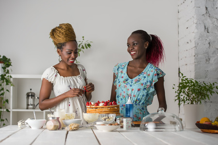 Young african women at the kitchen cooking cake with strawberryの写真素材