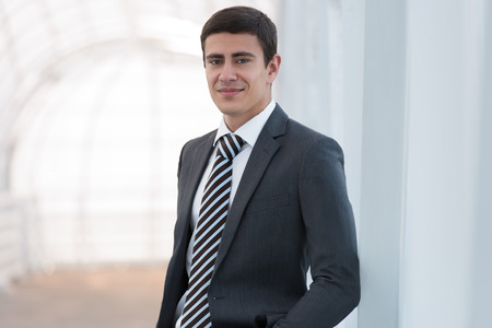 Portrait of handsome confident young businessman standing arms in pockets, smiling happy, looking at camera.の写真素材