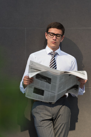 Handsome businessman or manager, in front of modern office architecture, reading newspaperの写真素材