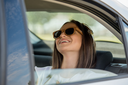 Young pretty girl wearing sunglasses listening music with headphones in car. Summer funの写真素材