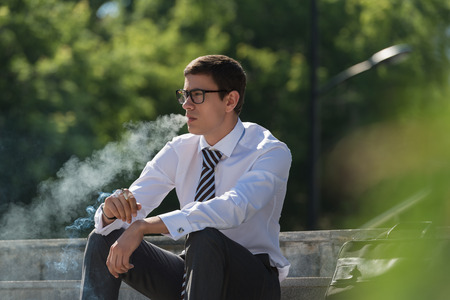 Well dressed business man smoking sitting on a street sidewalkの写真素材