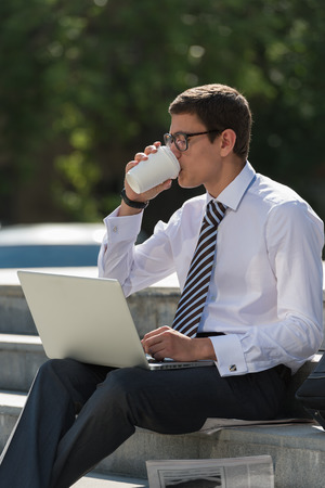 Man with laptop and coffee at summer park on bright dayの写真素材