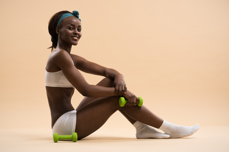 Beautiful african woman pumping up muscles with dumbbellsの写真素材