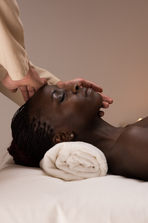 Beautiful young african woman enjoys facial massage in a luxury spa resortの写真素材