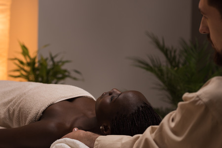 Beautiful young african woman enjoys shoulders massage in a luxury spa resortの写真素材
