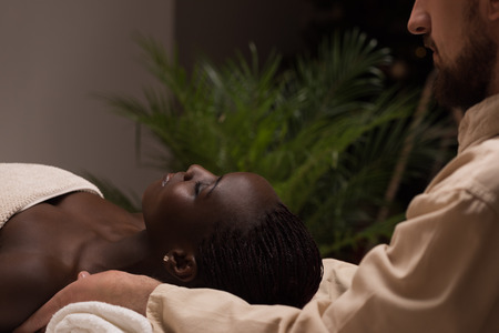 Beautiful young african woman enjoys shoulders massage in a luxury spa resortの写真素材