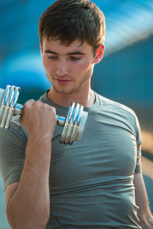 Athletic man pumping up muscles with dumbbells outdoors in cityの写真素材