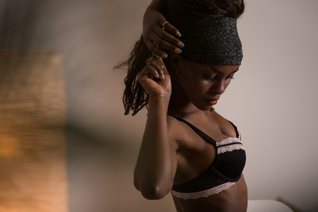 Beautiful alluring african woman in sexy lingerie. Portrait of beautiful sexy stylish young woman model with perfect clean skin in black lingerie posing at home through palm treeの写真素材