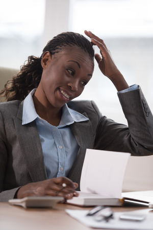 Young businesswoman sitting at workplace and writing numbers in notebook after calculating budgetの写真素材