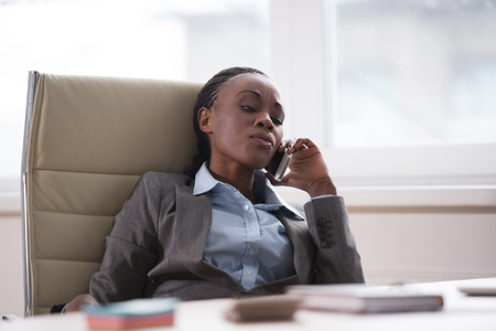 Businesswoman at workplace sitting relaxed and calling by phoneの写真素材