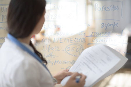 Medical doctor writing patient test results on transparent board to diagnoseの写真素材