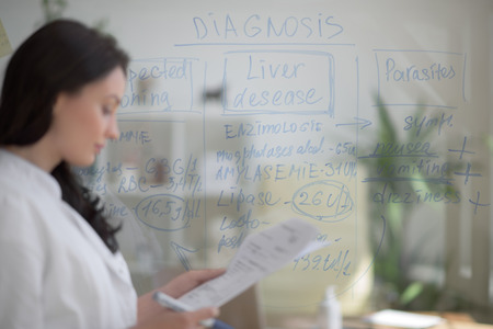 Medical doctor writing patient test results on transparent board to diagnose disease of her patientの写真素材