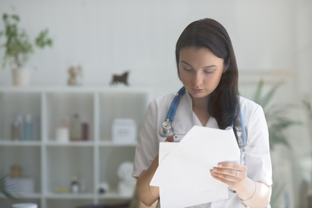 Doctor at her medical office using mobile phone and holding papers. View through the glassの写真素材