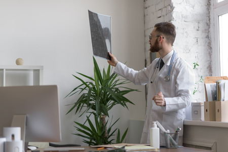 Closeup portrait of intellectual man healthcare personnel with white labcoat, looking at brain x-ray radiographic image, ct scan, mri, clinic office background. Radiology departmentの写真素材