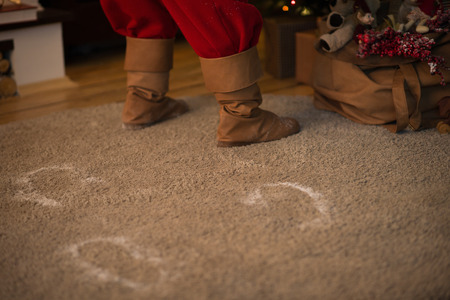 Santa Claus at Home putting gifts under Christmas Tree. Snow traces on carpetの写真素材