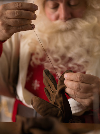 Santa Claus Working at Home. Repairing his Glovesの写真素材
