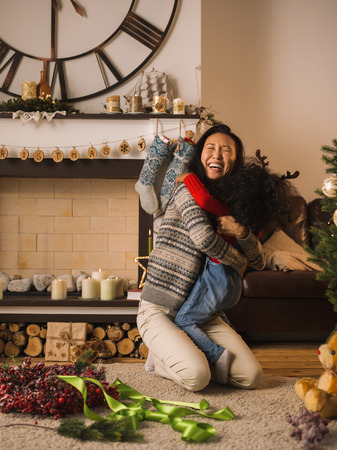 Mixed race mother and daughter hugging near Christmas treeの写真素材