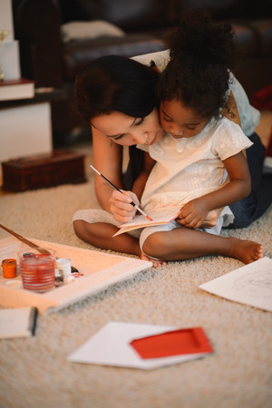 Mixed race mother and daughter playing and painting near Christmas tree at homeの写真素材