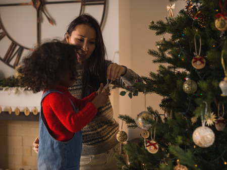 Mixed race mother and daughter decorating Christmas treeの写真素材