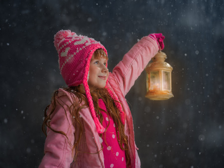 Little girl having fun under snow outside and lighting her way with lanternの写真素材