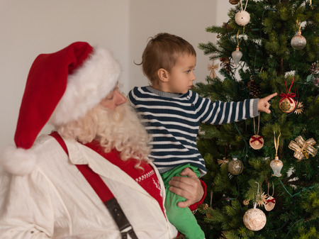 Santa Claus with Child Decorating Christmas Tree at Homeの写真素材