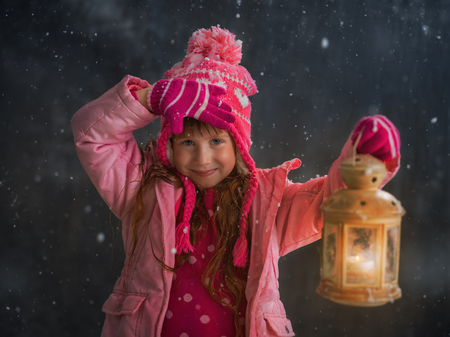 Little girl having fun under snow outside and lighting her way with lanternの写真素材