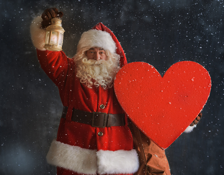 Photo of Santa Claus standing outdoors under snow and holding heartの写真素材