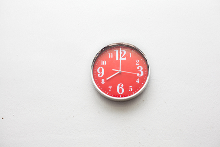 Red wall clock at  eight o'clock on white wall