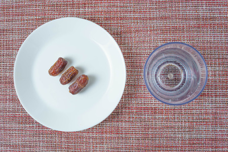 three dried dates on white plate with a glass of plain waterの写真素材