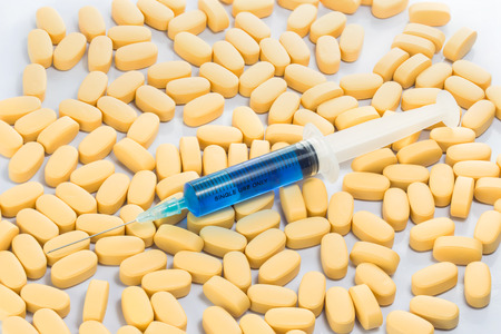 Syringe with blue serum above yellow pills isolated on white background