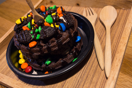 Chocolate waffles with sandwich cookie colorful button-shaped candies and chocolate syrup on wood plateの写真素材
