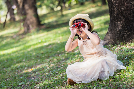 Little asian girl looking trough a binoculars in parkの写真素材