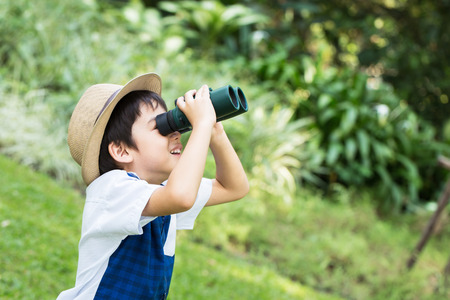 Little asian boy looking trough a binoculars with smiling face in parkの写真素材