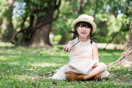 Little asian girl show pencil for writing book with smiling face in the parkの写真素材