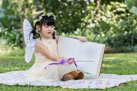 Little asian girl read book and point on book with smiling face in the parkの写真素材