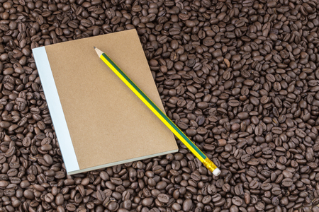 Paper notebook and pencil on roasted coffee seed backgroundの写真素材